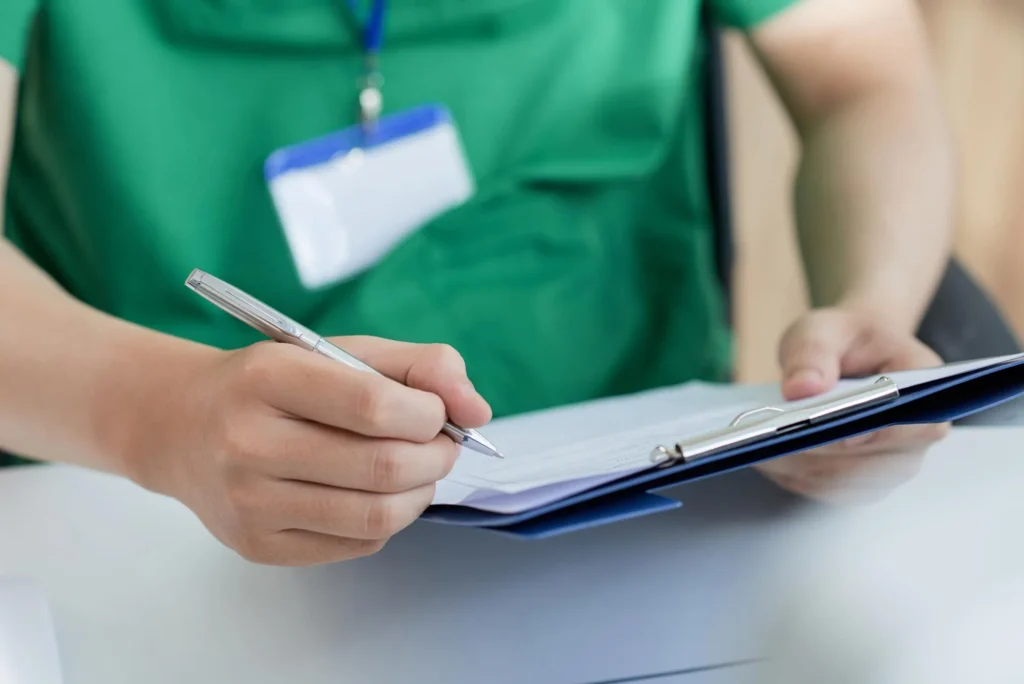 A nurse writing on a note pad with a pen and paper