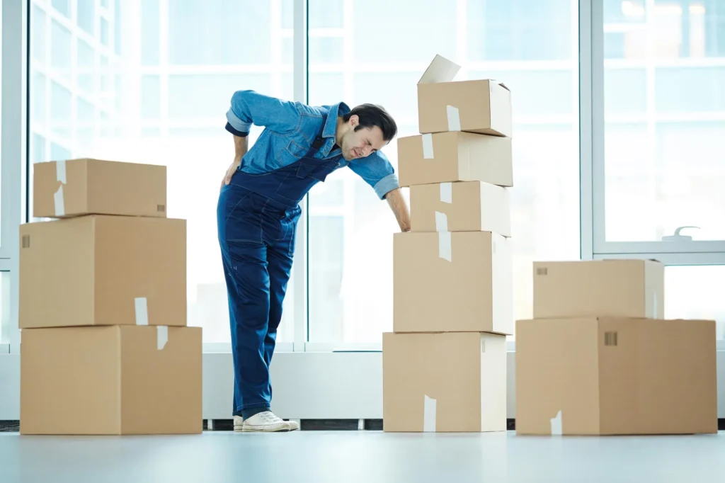 Man moving boxes hunched over holding his back in pain