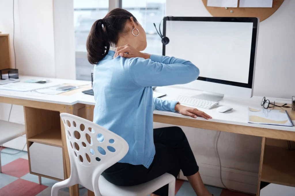 woman working at her desk self-soothing her neck and back pain