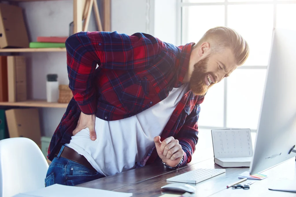 Man feeling pain in his lower back holding his back at his work desk