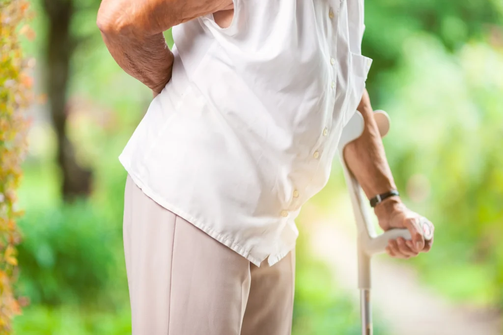 An image of an elderly person holding their back while walking with a cane