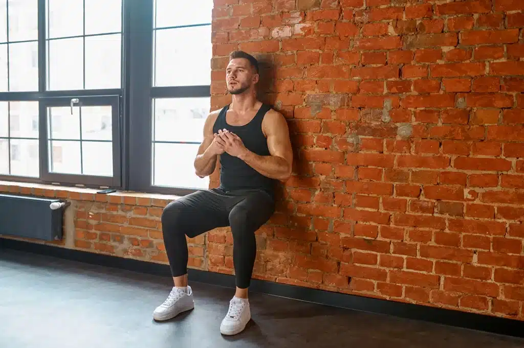 Athletic young man doing wall squat exercise for the spine