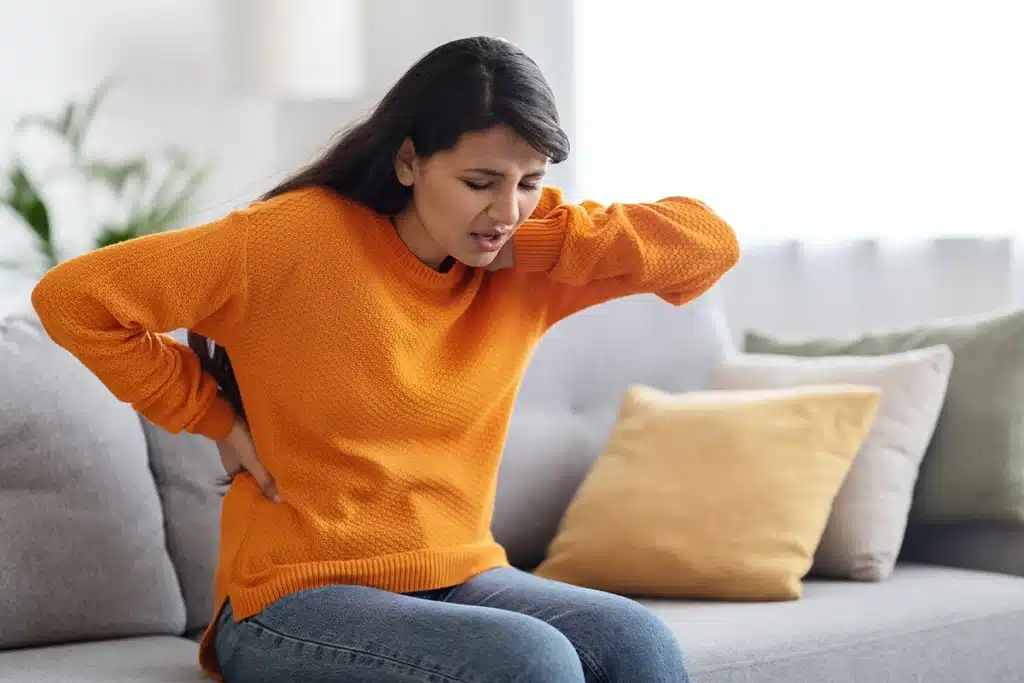Woman sitting on a sofa holding her back in pain