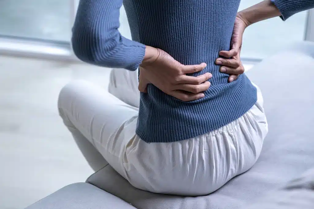Woman sitting on a sofa holding her lower back in pain
