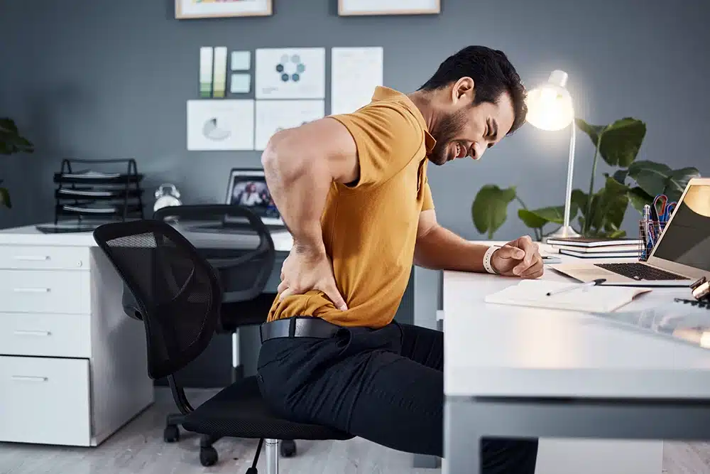 Man sitting at his desk holding his lower back in pain