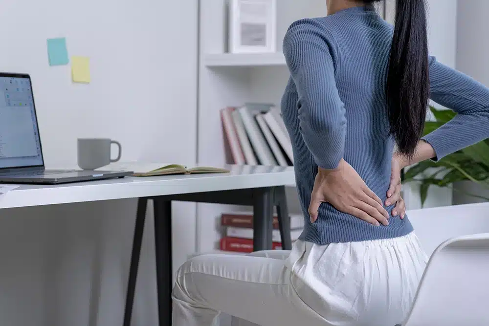 A woman at her home office holding her back in pain