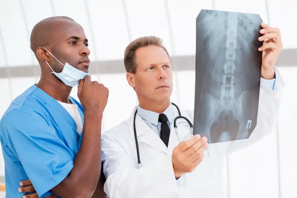 Two surgeons analyzing an X-ray image to plan minimally invasive spine surgery in a modern medical facility.