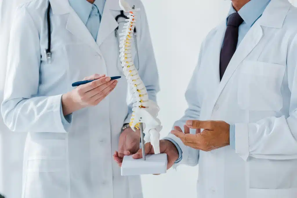 Close-up view of a doctor holding a spine model and explaining spine anatomy and surgery options to a patient.