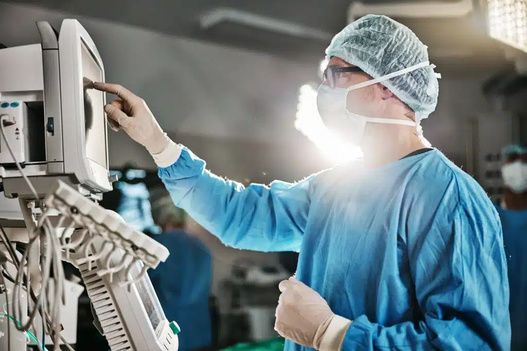 Doctor in surgical attire using a monitor and medical equipment in an operating theater.