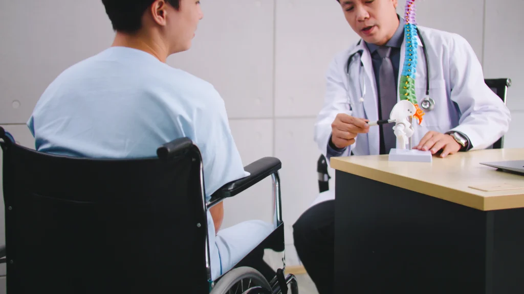 Doctor explaining spinal anatomy to patient in a wheelchair, focusing on spinal fusion surgery and disability rating.