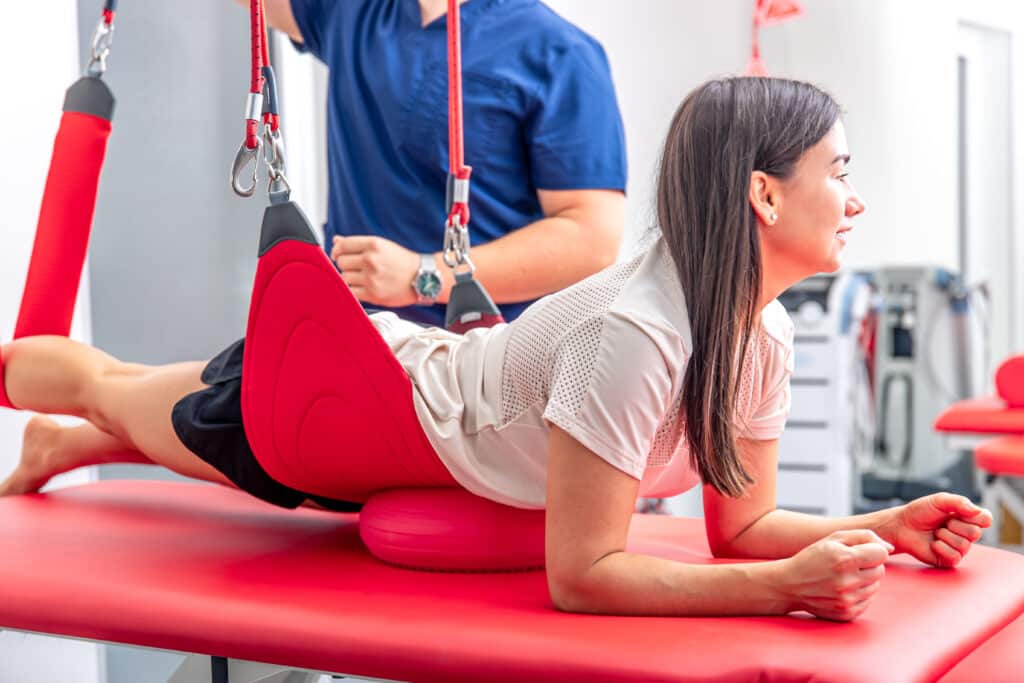 A young woman performs guided exercises using ropes to restore mobility following spinal fusion surgery.