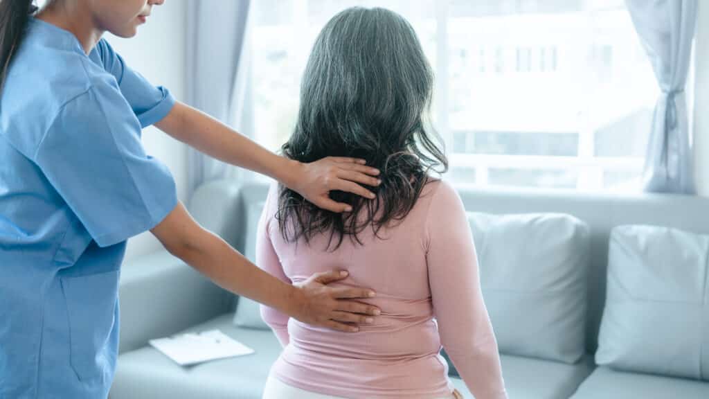 Female physiotherapist assessing patient’s back during spinal fusion recovery.