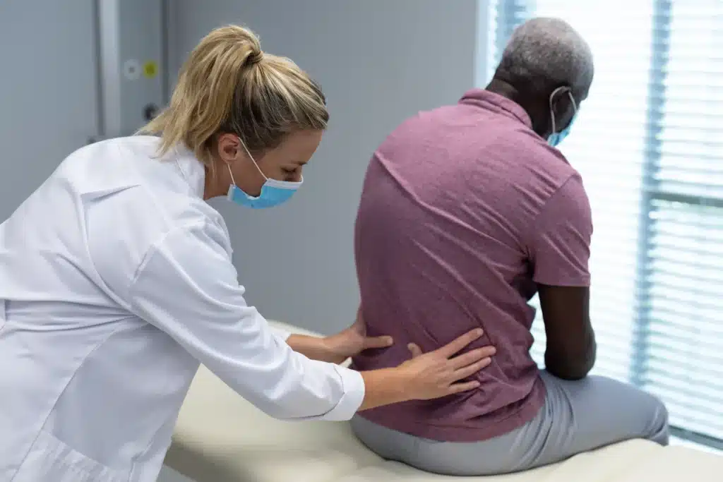 Physiotherapist evaluating back pain in patient during post-spinal fusion physical therapy.