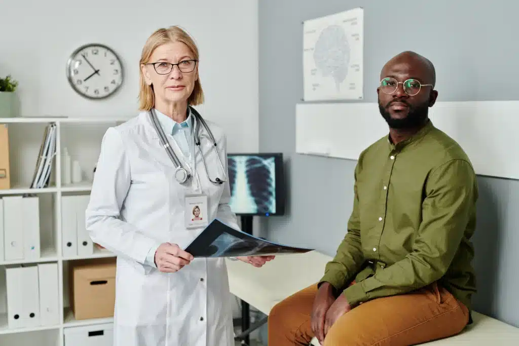 Doctor holding an X-ray explaining spinal fusion complications to a patient in a medical consultation room