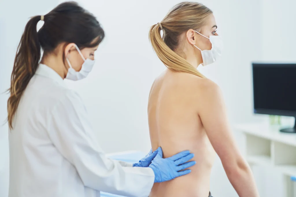 Doctor examining a patient’s spine after spinal fusion surgery for scar assessment.