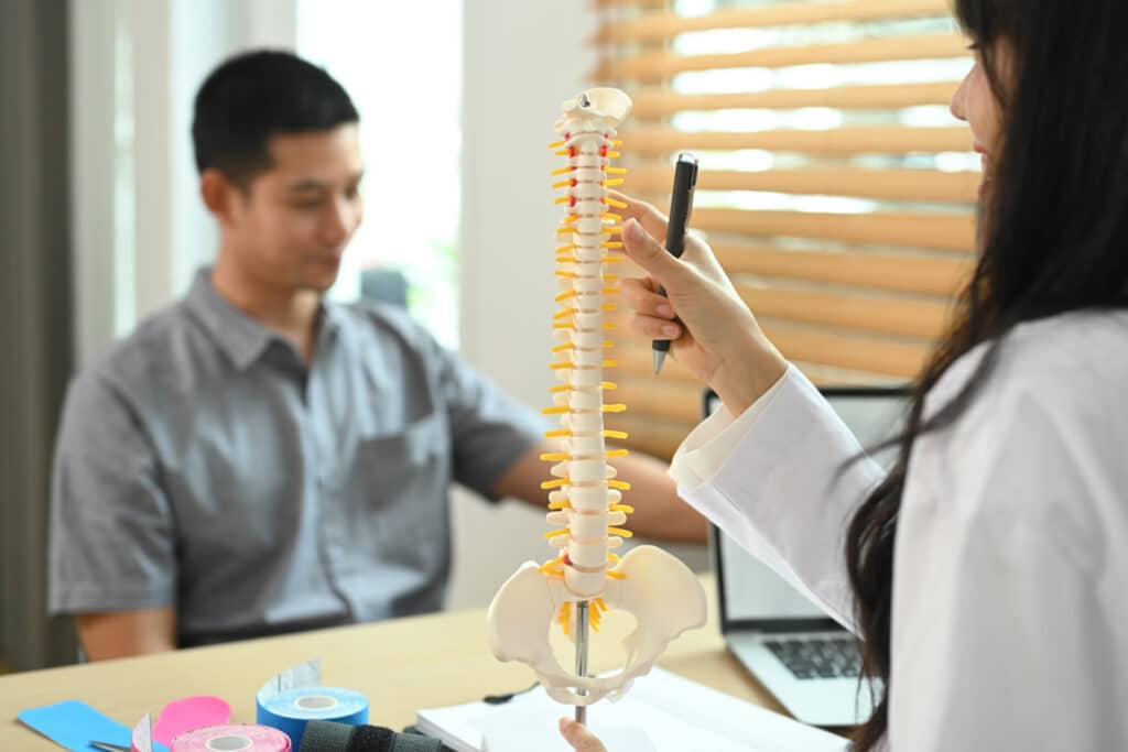 A physical therapist explains post-op spine care using a model, guiding a patient through spinal fusion recovery protocols.