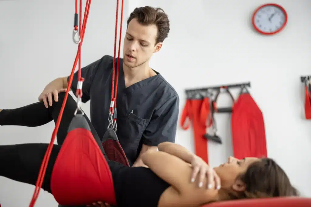 Physical therapist helping a patient with suspended leg exercises to aid recovery after spinal fusion surgery.