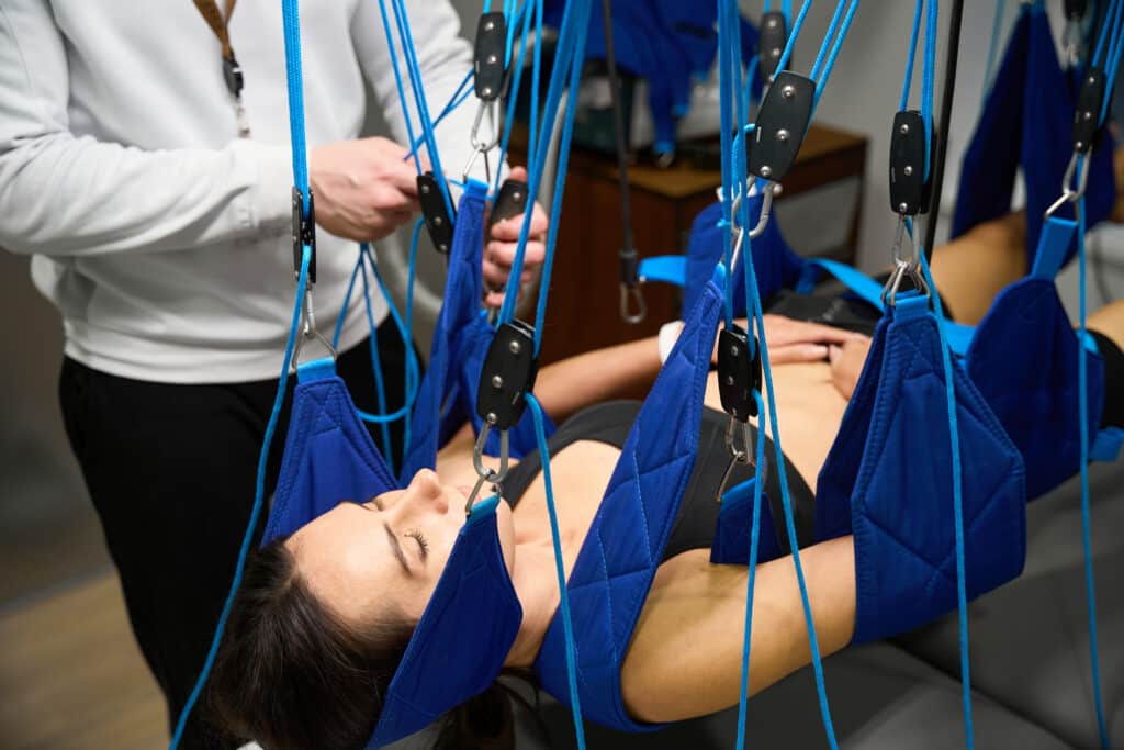 woman undergoing sling therapy as part of her post-operative spinal fusion rehabilitation, focusing on improving mobility and core strength.