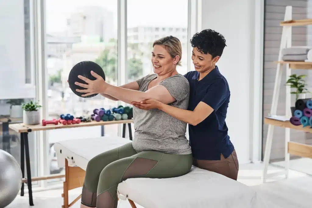 Therapist assisting a patient with a stability ball exercise to strengthen core muscles after spinal fusion.