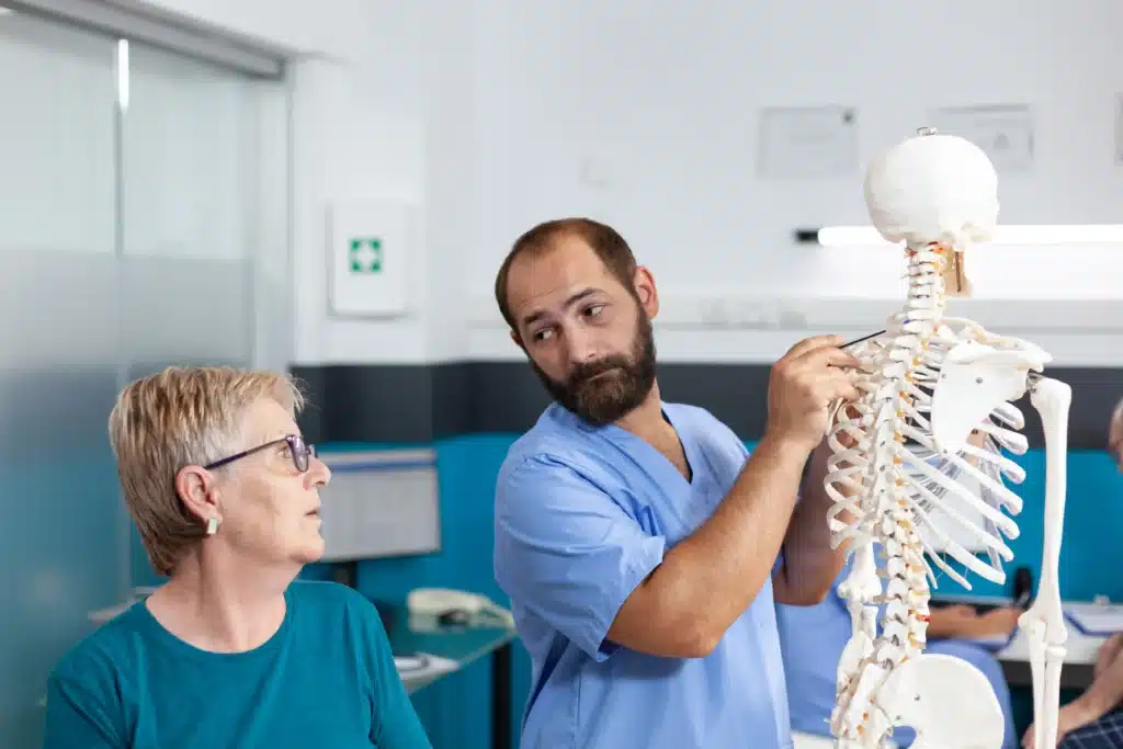 A healthcare professional explaining spinal fusion surgery using a spine model to a patient.