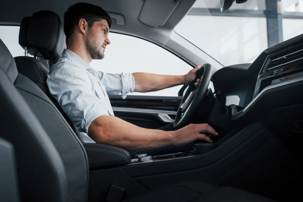 Young man adjusting his posture in a car to prevent back pain from driving.