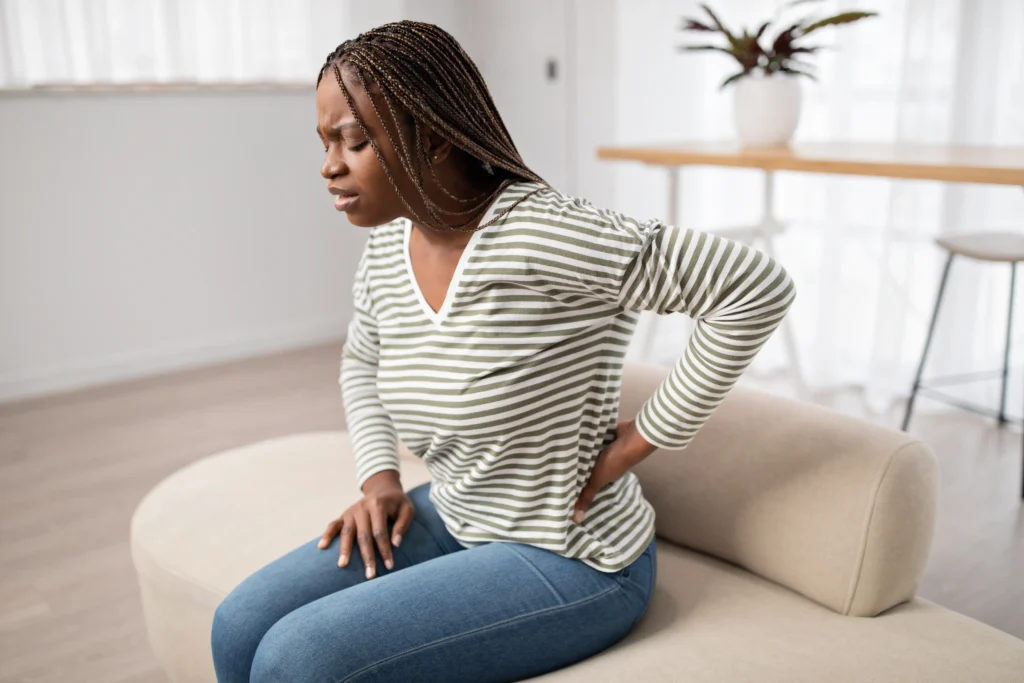 A woman experiencing chronic back pain while sitting on a couch, representing the challenges of living with physical discomfort.