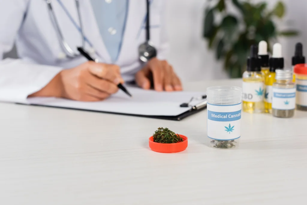 A doctor writing a prescription with a container of medical cannabis and cannabis products on the table.