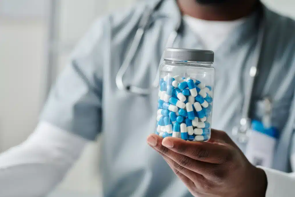 Doctor holding a jar of blue and white opioid capsules used for severe pain relief.