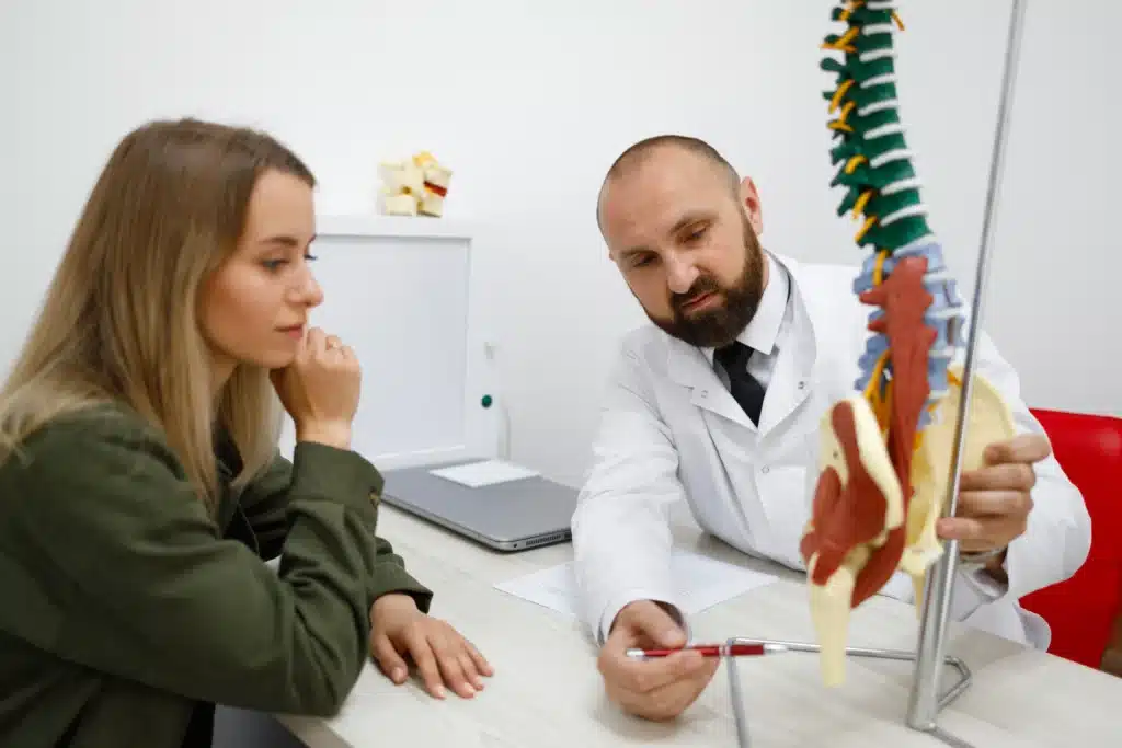 "Doctor explaining spine model to patient discussing spine surgery insurance coverage options.