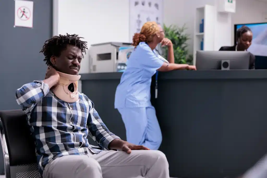 Man wearing a cervical neck collar, seated at a reception desk, waiting for treatment options like injections for cervical neck pain.