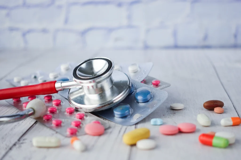 A stethoscope with various medical pills and blister packs on a wooden table.