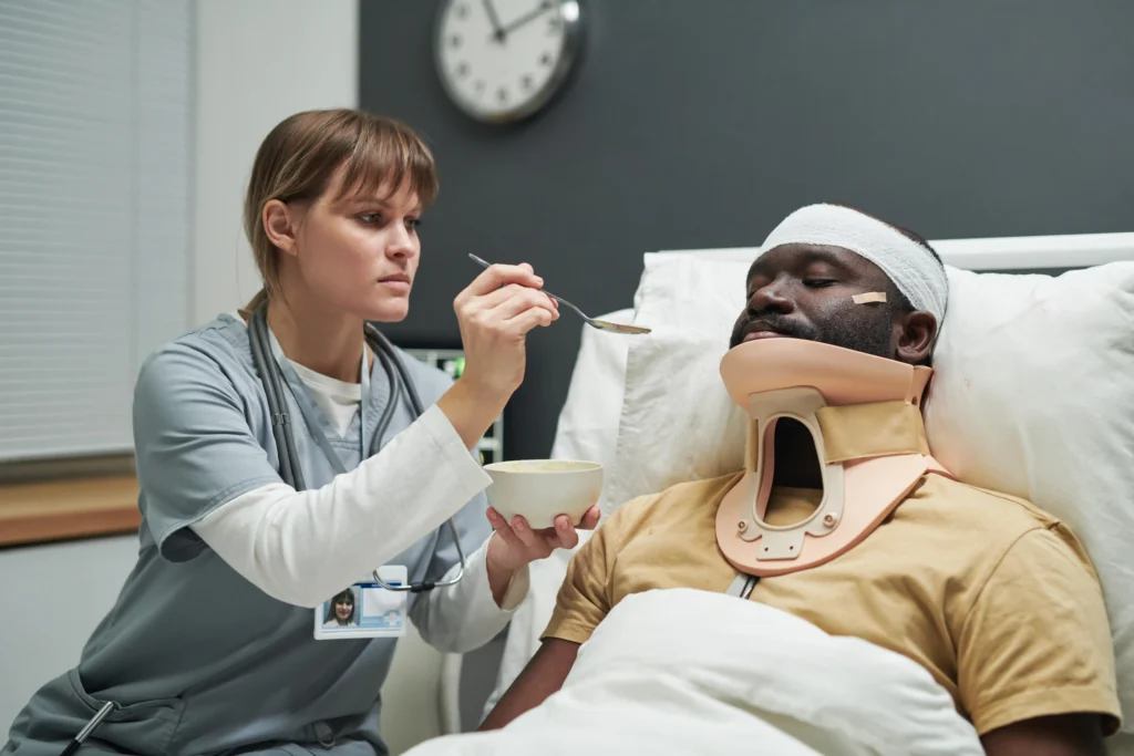 Nurse feeding a patient in a neck brace with porridge, supporting recovery after surgery.