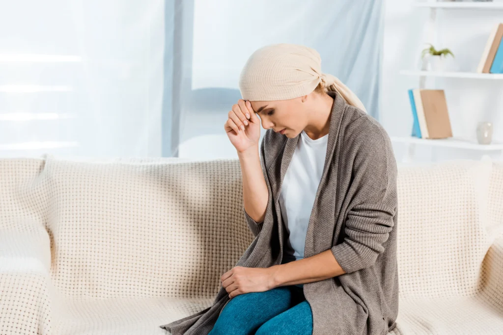 Woman with a headscarf sitting on a couch, reflecting on the challenges of managing oncological pain.