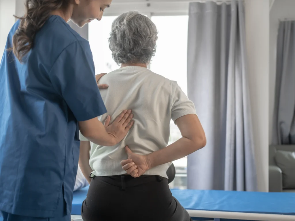 Nurse assisting senior woman with spinal discomfort, symbolizing spinal fusion failure symptoms.