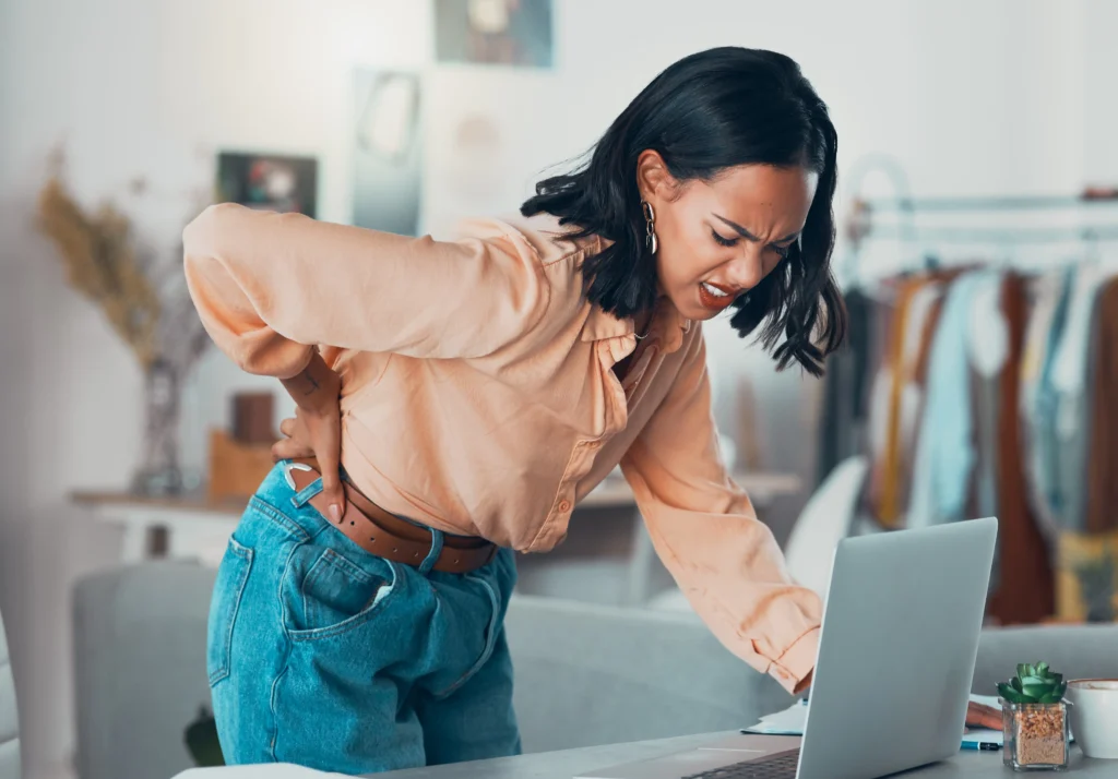 Designer experiencing sharp back pain while working, illustrating the symptoms of back pain vs kidney stone discomfort.