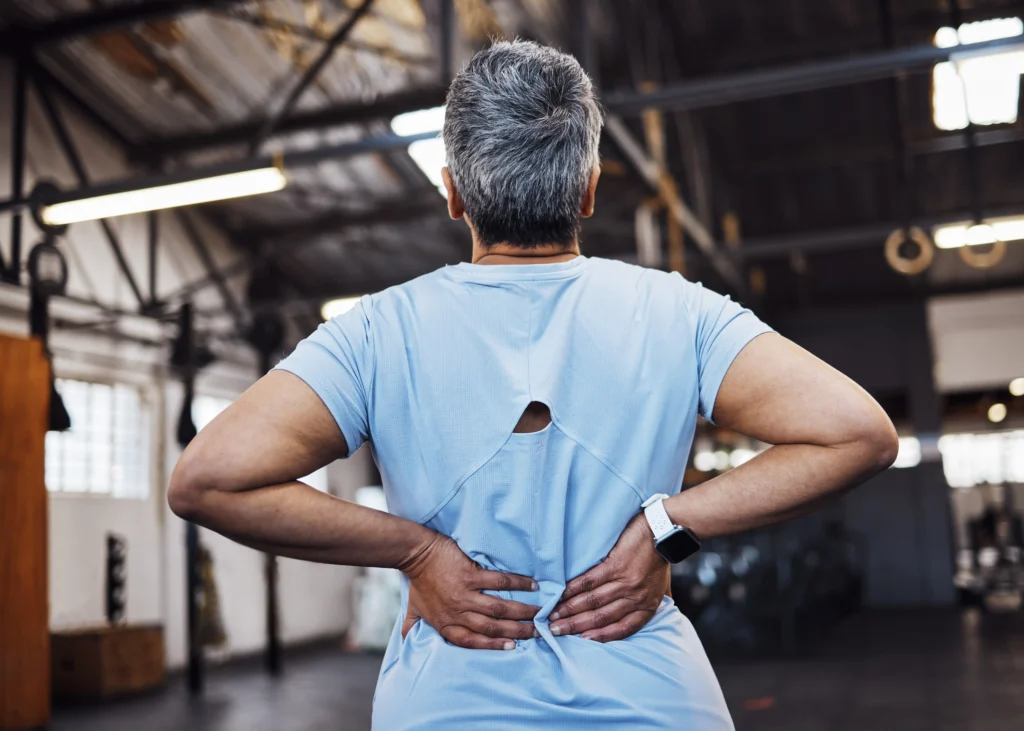 Woman holding lower back in gym, representing spinal pain and fusion failure symptoms.