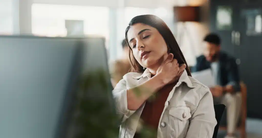 Businesswoman experiencing neck pain while working in an office, showcasing the need for McKenzie Method exercises.