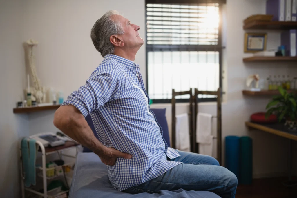 Senior male patient experiencing back pain in a medical setting, illustrating spinal fusion failure symptoms.