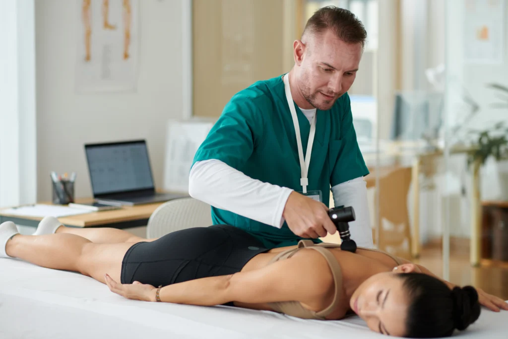 Therapist using a massage gun for back pain relief as part of SI joint pain treatment in Long Island.