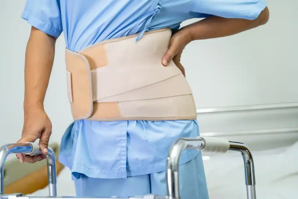 A patient using a walker and wearing a back support belt after spinal surgery, addressing spinal fusion failure symptoms.