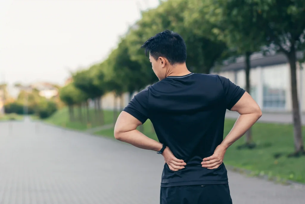 An athletic man holding his lower back while walking outdoors, emphasizing the importance of staying active for back pain relief fast through gentle movement and posture awareness.