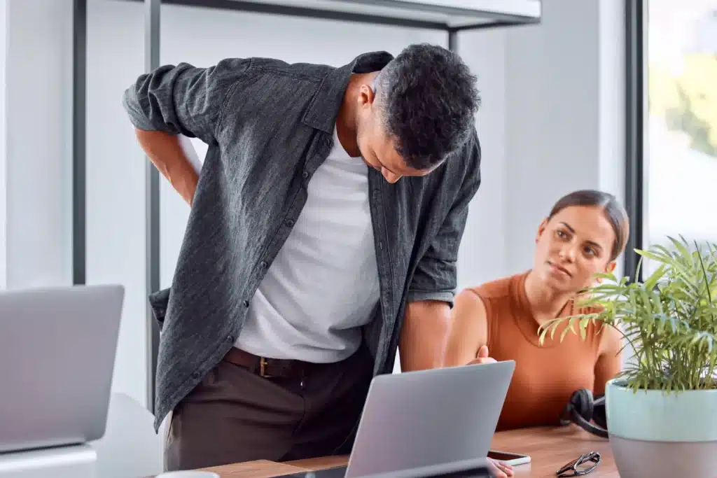 A man experiencing back pain in the office, a potential sign of spinal fusion failure symptoms.