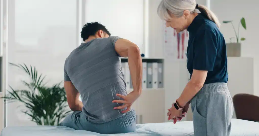 Patient holding their lower back during a physical therapy consultation with a healthcare professional.