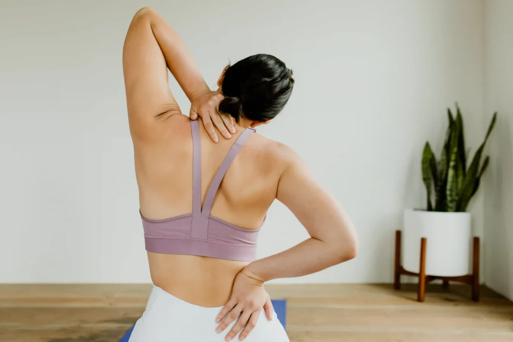 Back view of a fitness woman reaching her back during a neck pain relief yoga session.