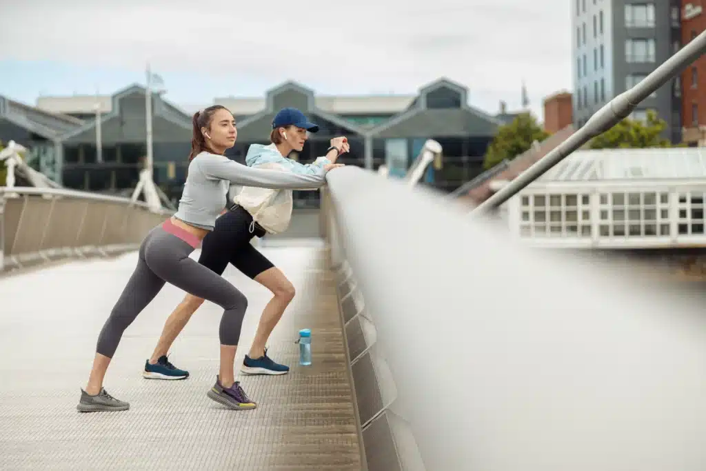 Two women performing stretching exercises on a pedestrian bridge for improved posture and muscle flexibility.