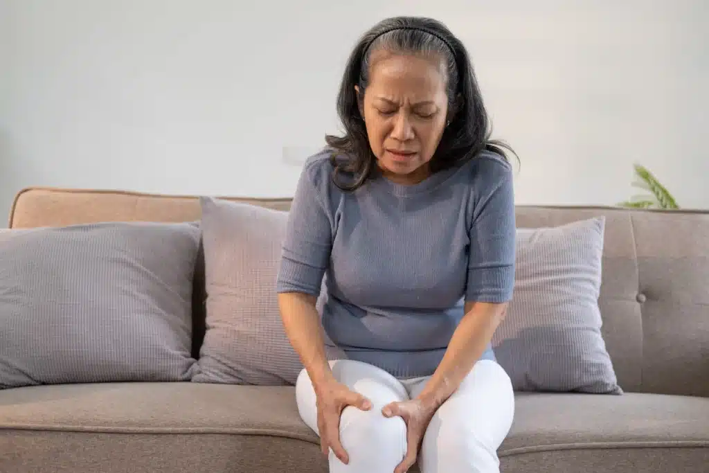 An elderly woman massaging her knee, illustrating the need for effective SI joint pain treatment in Long Island.