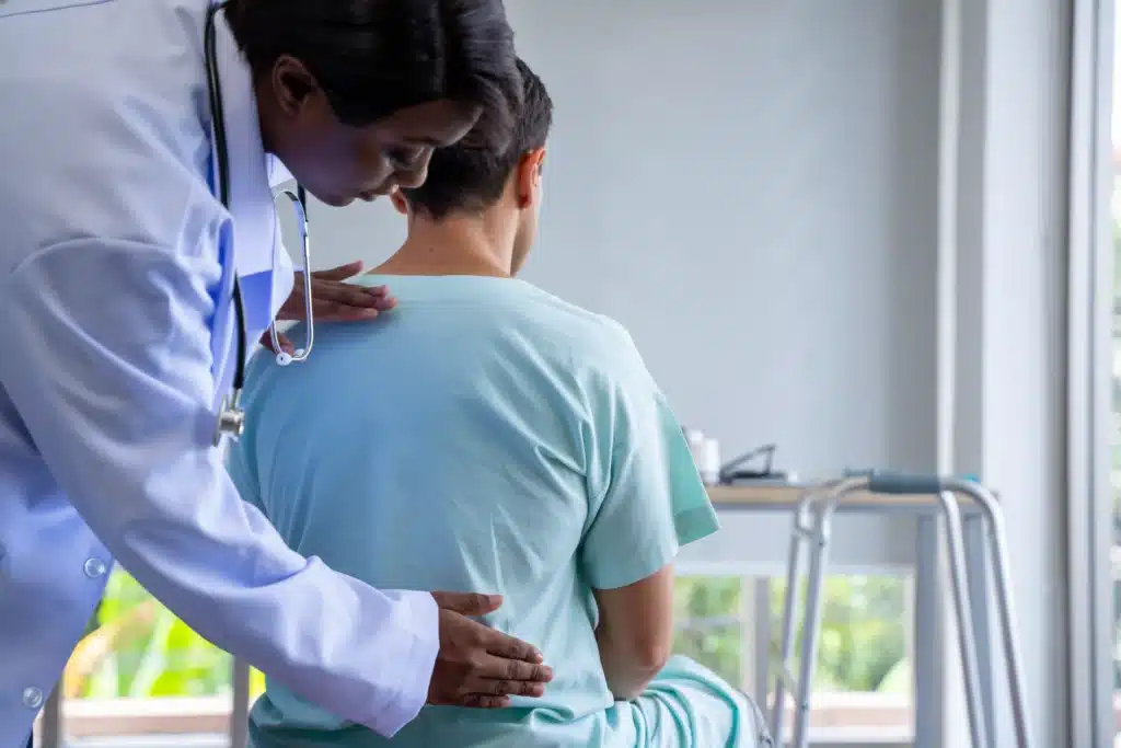 Female doctor examining a male patient's upper back during a physical therapy session.