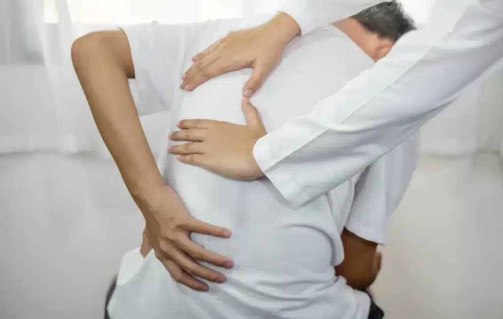 Physiotherapist assisting a patient by applying pressure to relieve back pain during a treatment session.