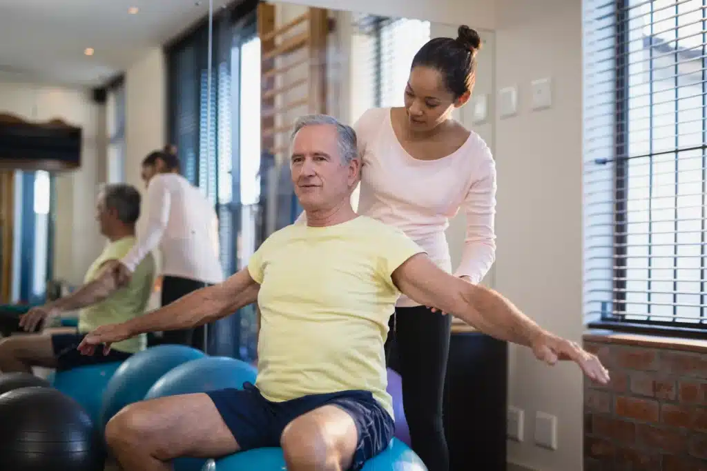 Physical therapist assisting a male patient with spinal fusion exercises on a stability ball.