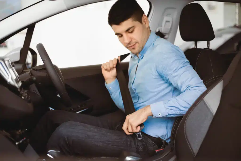 Man sitting in a car fastening his seatbelt with a focused expression.